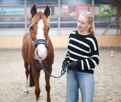 Junge Frau hält ein Pferd am Führstrick bei der Bodenarbeit